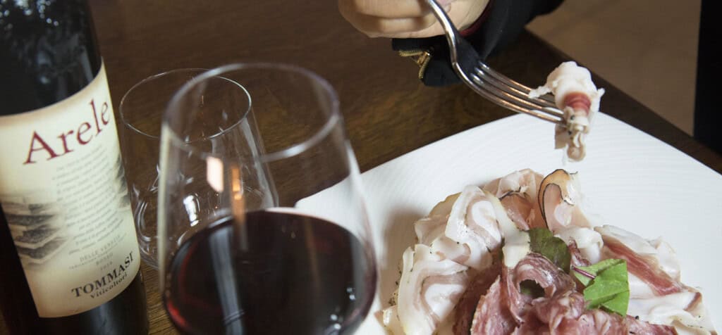 En tallrik med skinka, ett glas rött vin och en flaska Amarone,