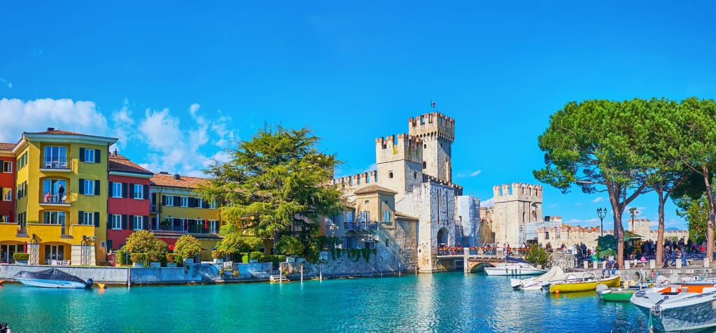 Den natursköna marinan i Sirmione med Gardasjöns azurblå vatten, färgade hus, Scaligero slott och utbredda gröna tallar, Sirmione, Italien